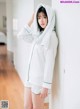 A woman in a white hooded sweatshirt and shorts leaning against a wall.