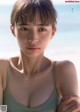 A woman in a green tank top standing on a beach.