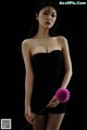 A woman in a black dress holding a pink flower.